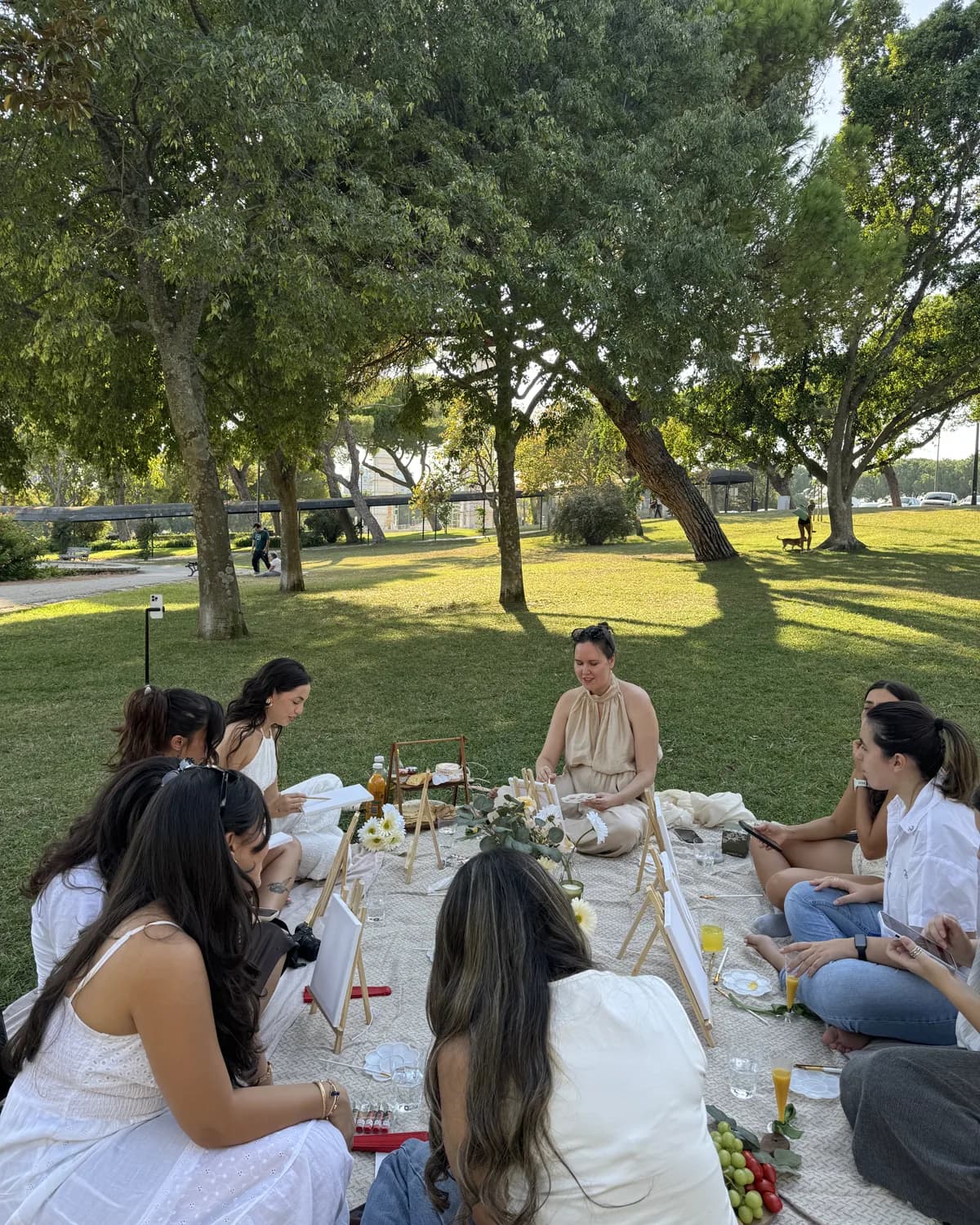 Women seated around a picnic blanket with canvases and easels in a Lisbon park