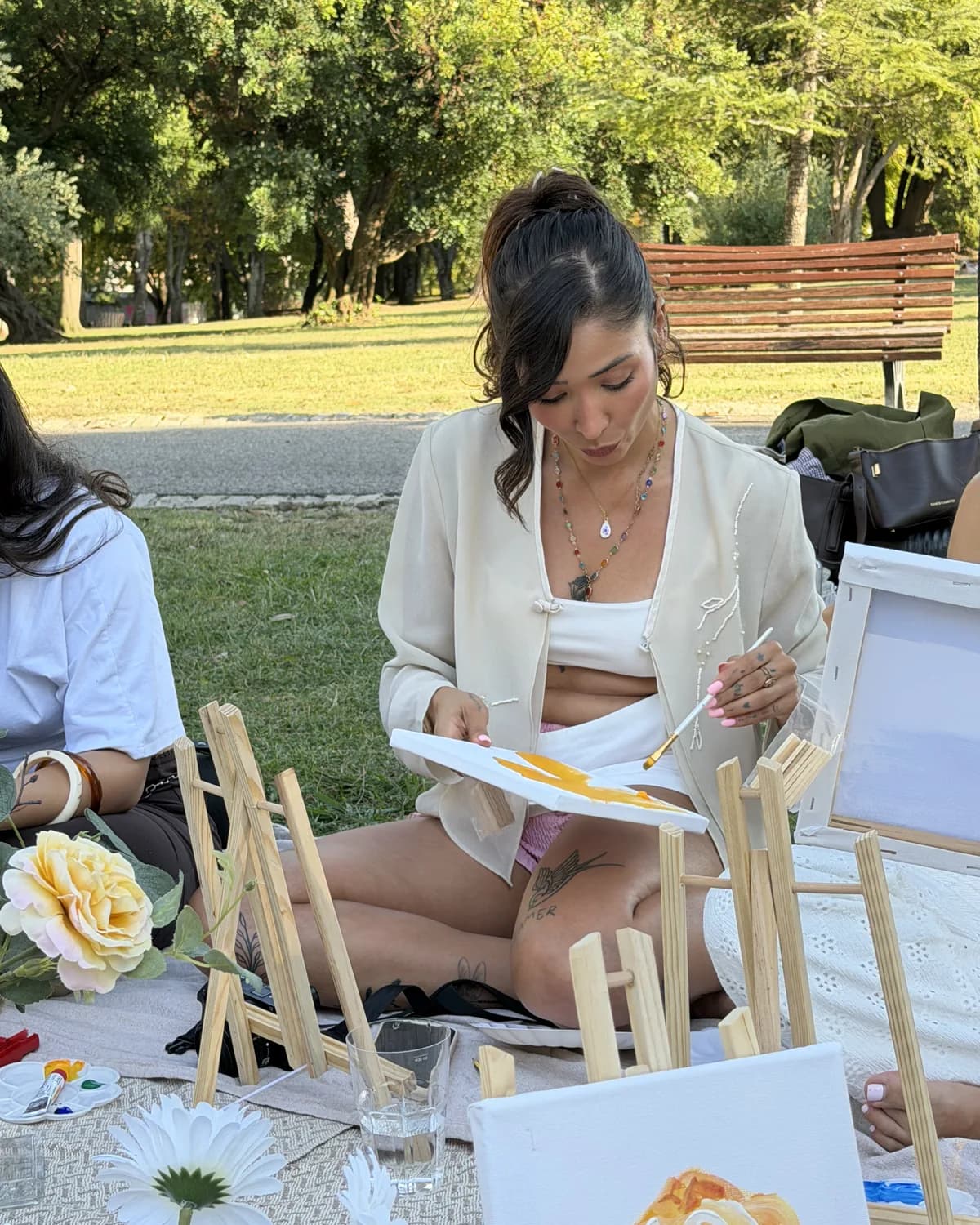 A woman painting a yellow canvas while seated among small easels in a Lisbon park