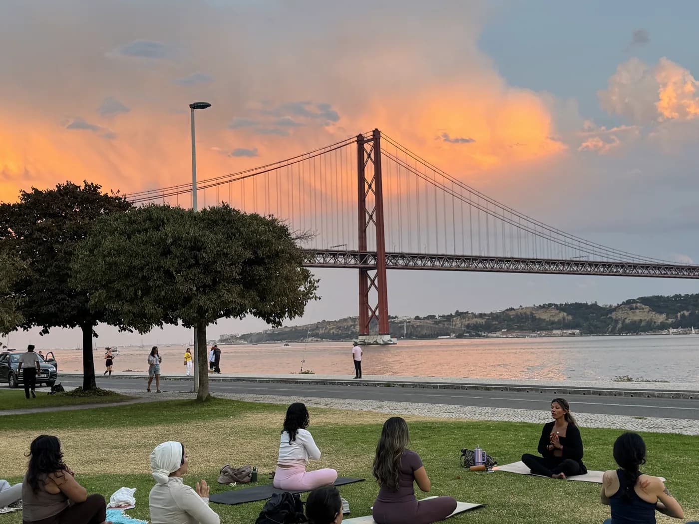 Women seated on yoga mats at sunset beside the river and Lisbon bridge