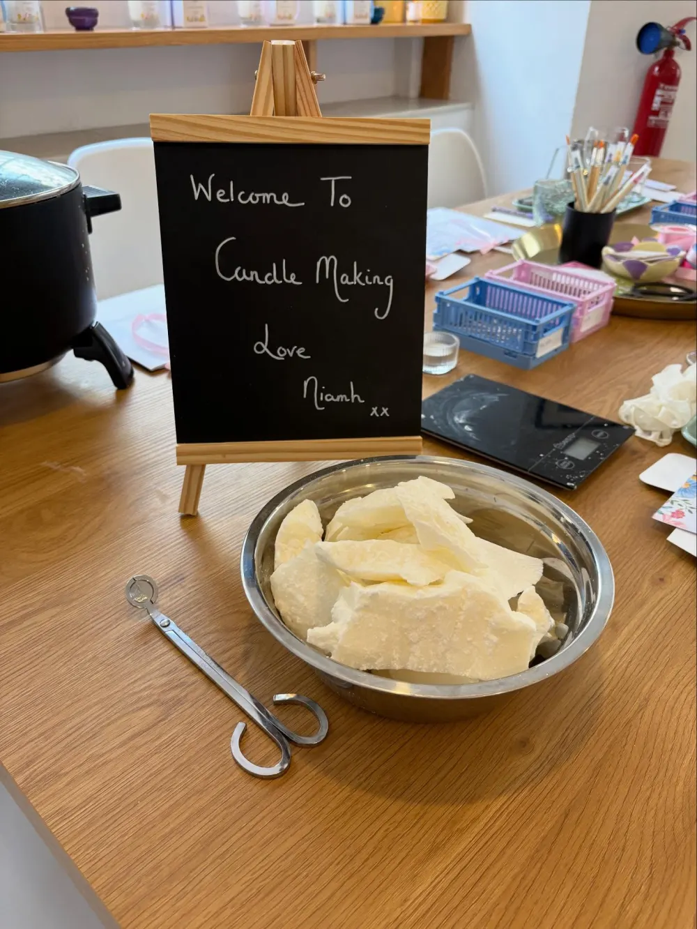A chalkboard reading “Welcome to Candle Making, love Niamh” beside a bowl of wax flakes